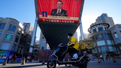 A delivery courier rides past a large video screen at a shopping mall showing Chinese Premier Li Keqiang speaking during the opening session of the annual meeting of China's National People's Congress (NPC) in Beijing, Saturday, March 5, 2022.