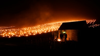 Winegrowers warm themselves around a fire as anti-frost candles burn in a vineyard, Chablis, France, April 4, 2022.