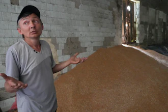 A farmer gestures near a mound of grain in his barn in Ptyche, Ukraine, June 12, 2022.