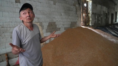 A farmer gestures near a mound of grain in his barn in Ptyche, Ukraine, June 12, 2022.