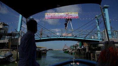 Fisherman Ng Koon-hee sails past a bridge where a worker hangs a banner to mark the 25th anniversary of Hong Kong's return to Chinese rule, June 25, 2022.