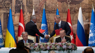 Turkish President Recep Tayyip Erdogan, right, and U.N. Secretary General, Antonio Guterres, sit as two representatives of Ukraine and Russia delegations check hands during a signing ceremony at Dolmabahce Palace, Istanbul, July 22, 2022.