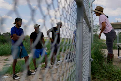 Magali Urbina, right, talks through her fence to migrants who crossed the Rio Grande illegally at her pecan farm, Heavenly Farms, Aug. 26, 2022, Eagle Pass, Texas.