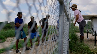 Magali Urbina, right, talks through her fence to migrants who crossed the Rio Grande illegally at her pecan farm, Heavenly Farms, Aug. 26, 2022, Eagle Pass, Texas.