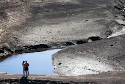 A couple stands on an ancient packhorse bridge exposed by low water levels at Baitings Reservoir, Ripponden, England, Aug. 12, 2022.