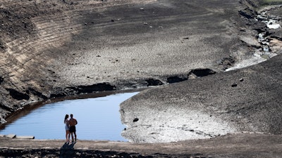A couple stands on an ancient packhorse bridge exposed by low water levels at Baitings Reservoir, Ripponden, England, Aug. 12, 2022.