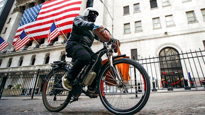 A delivery worker rides his electric bicycle past the New York Stock Exchange, March 16, 2020, in New York. New York City's thousands of food delivery workers will get places to recharge electric bike batteries, cellphones and themselves, under a city plan announced Monday, Oct. 3, 2022, to turn abandoned newsstands and other unused structures into facilities for the 'deliveristas.'