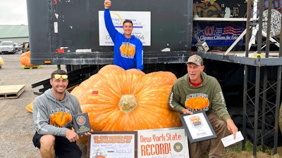 In this photo provided by The Great Pumpkin Farm, Emmett Andrusz, from left, Steve Andrusz and Scott Andrusz, pose with the record setting 2,554-pound pumpkin, in Clarence, N.Y., Saturday, Oct. 1, 2022. Scott Andrusz's entry broke the previous record of 2,528 pounds.