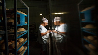 Svitlana Labutcheva, cuts labels by hand for packaging loaves of bread at a bakery in Kostiantynivka, Donetsk region, eastern Ukraine, Saturday, Aug. 20, 2022. Seemingly abandoned during the day, the damaged factory building in eastern Ukraine comes to life at night, when the smell of fresh bread emanates from its broken windows.