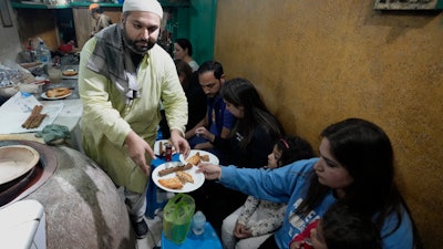 Bilal Sufi, left, owner of Baking Virsa eatery, serves kebabs and naan bread in Lahore, Pakistan, Dec. 3, 2022.