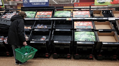 A customer checks almost empty fruit and vegetable shelves at an Asda in east London, Feb. 21, 2023.