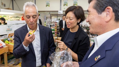 U.S. Ambassador to Japan Rahm Emanuel, left, eats a fig at JA farmer’s market in Soma, Japan, Aug. 31, 2023.