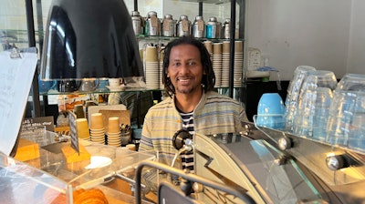 Anteneh Mulu, 46, poses behind the counter after serving a customer at his coffee shop, The Ethiopian Coffee Company, in central London on Thursday, Aug. 31, 2023. Mulu and his business partner Polly Hamilton, 79, opened their shop in 2013. The London-based International Coffee Organization has declared this Sunday, Oct. 1, as International Coffee Day.