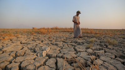 A fisherman walks across a dry patch of land in the marshes in Dhi Qar province, Iraq, Sept. 2, 2022.