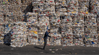 A GreenNet recycling plant employee cleans the ground next to piles of disposable plastic ready for export, in Atarot industrial zone, north of Jerusalem, Jan. 25, 2023.