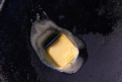 A pat of butter derived through a chemical process melts in a pan.