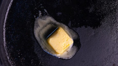 A pat of butter derived through a chemical process melts in a pan.