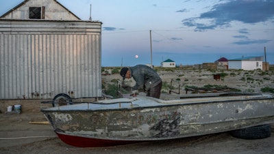 A man repairs an old boat along the dried-up Aral Sea, Tastubek, Kazakhstan, July 2, 2023.