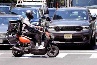 A delivery driver on a scooter rides the pedestrian crosswalk.