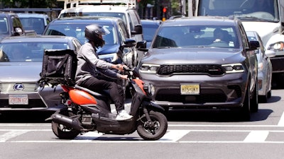 A delivery driver on a scooter rides the pedestrian crosswalk.