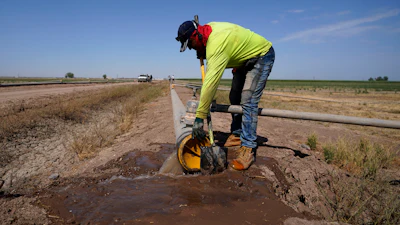A worker diverts water as a sprinkler system is installed for alfalfa at the Cox family farm near Brawley, Calif., Aug. 15, 2022.