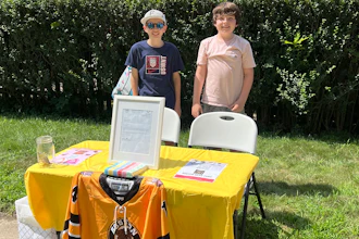 Ben Doherty, 12, of Braintree, Mass., left, stands with his cousin Danny Doherty, 12, of Norwood, Mass., right, near a table for donations to the Boston Bear Cubs hockey team, in Norwood.