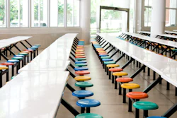 Clean school cafeteria with many empty seats and tables.