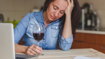 A woman showing signs of headache whilst drinking red wine.