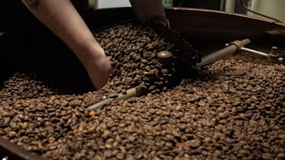 Renee Colon lifts coffee beans from the cooling tray of a roasting machine at Fuego Coffee Roasters' roasting facility, Rochester, N.Y., March 21, 2025.