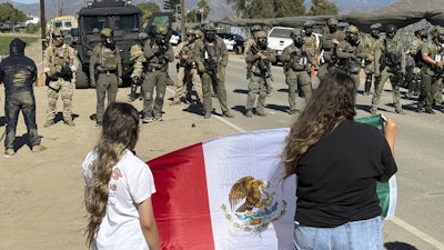 Demonstrators hold a flag in front of federal agents blocking a road during an immigration raid in Camarillo, Calif.