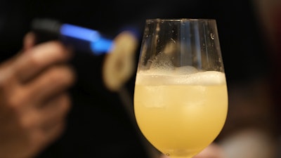 A bartender applies heat to a slice of dried pear as he prepares a cocktail named 'Beijing Beijing' at a bar in Beijing, June 13, 2025.