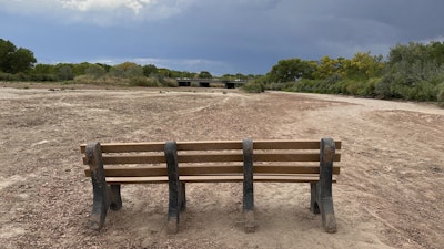 A park bench sits in the dry riverbed of the Rio Grande as traffic crosses a bridge along historic Route 66 in Albuquerque, N.M., on Thursday, Aug. 21, 2025.