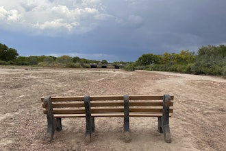 A park bench sits in the dry riverbed of the Rio Grande as traffic crosses a bridge along historic Route 66 in Albuquerque, N.M., on Thursday, Aug. 21, 2025.