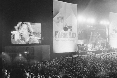 John Cougar Mellencamp performs both on stage and on one of two large screen television screens set up at the University of Illinois Memorial Stadium in Champaign, Ill. on Sept. 22, 1985 during the Farm Aid concert.