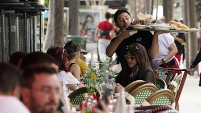 A waiter delivers food to patrons at a restaurant, Jan. 21, 2022, in Miami Beach, Fla.