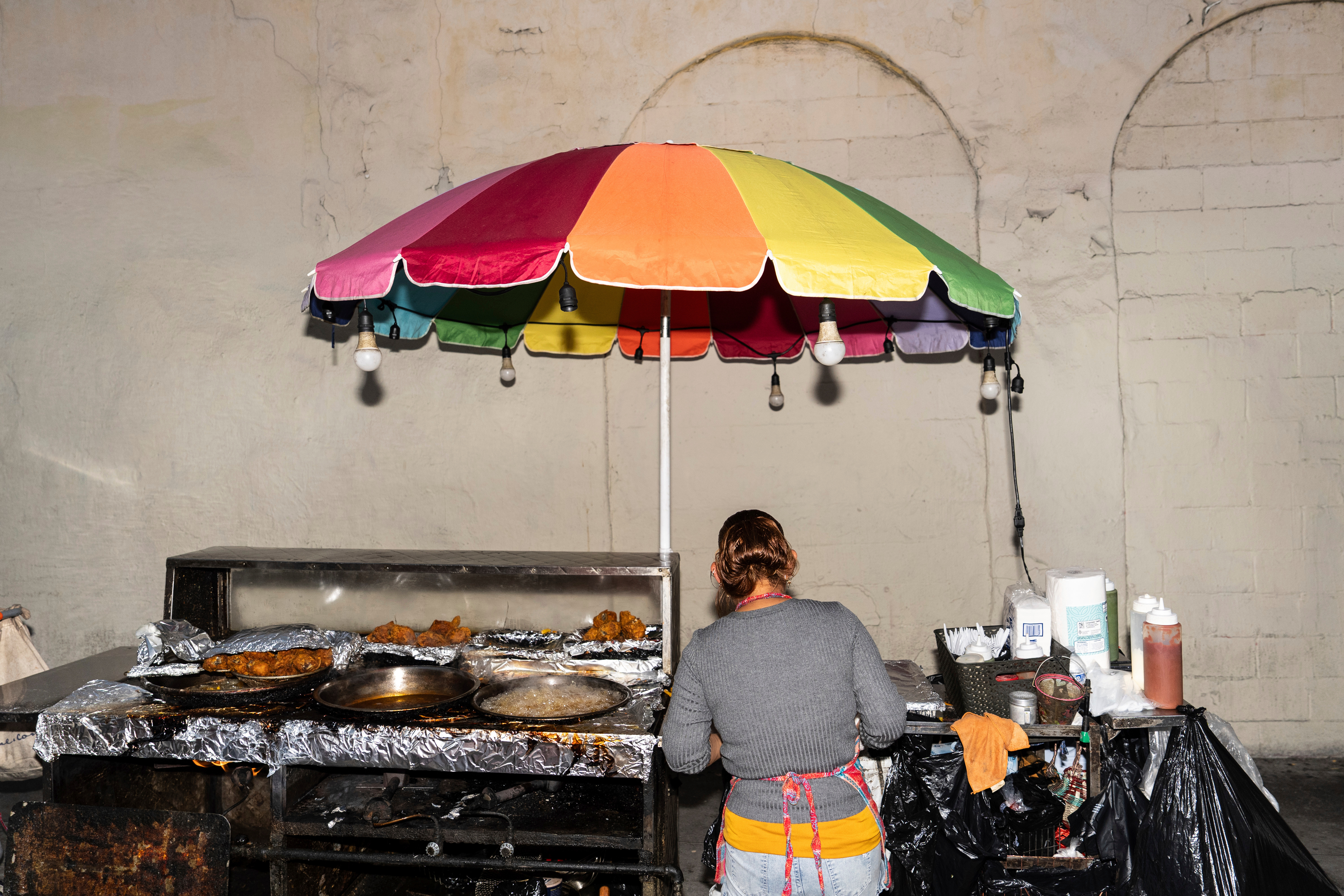 Street vendor Francisca, an immigrant from Guatemala, prepares an order at her cart in Los Angeles, Tuesday, Aug. 5, 2025, where her son accompanies her to help monitor their surroundings amid ongoing ICE raids.