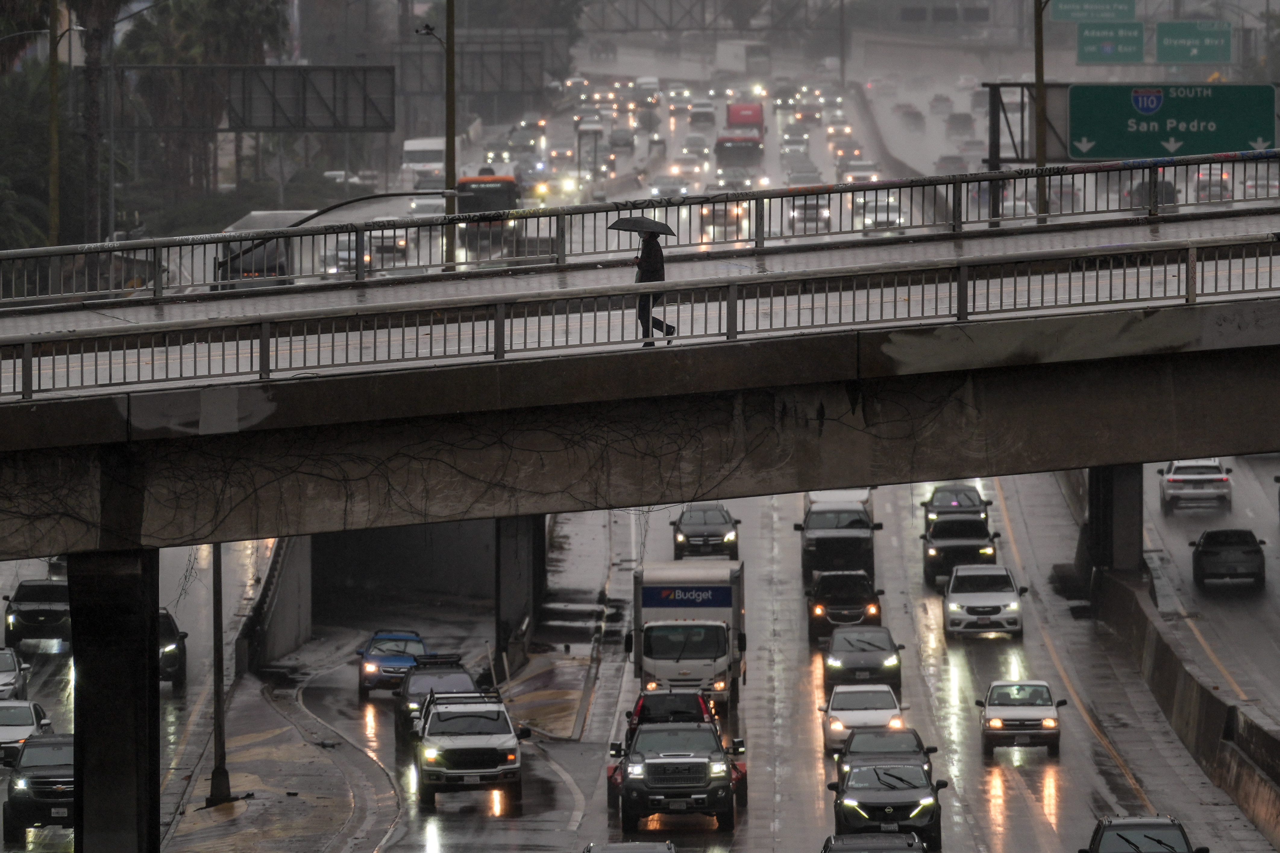 A pedestrian with an umbrella walks on a bridge over the rain-soaked 110 Freeway in Los Angeles, Nov. 14, 2025.