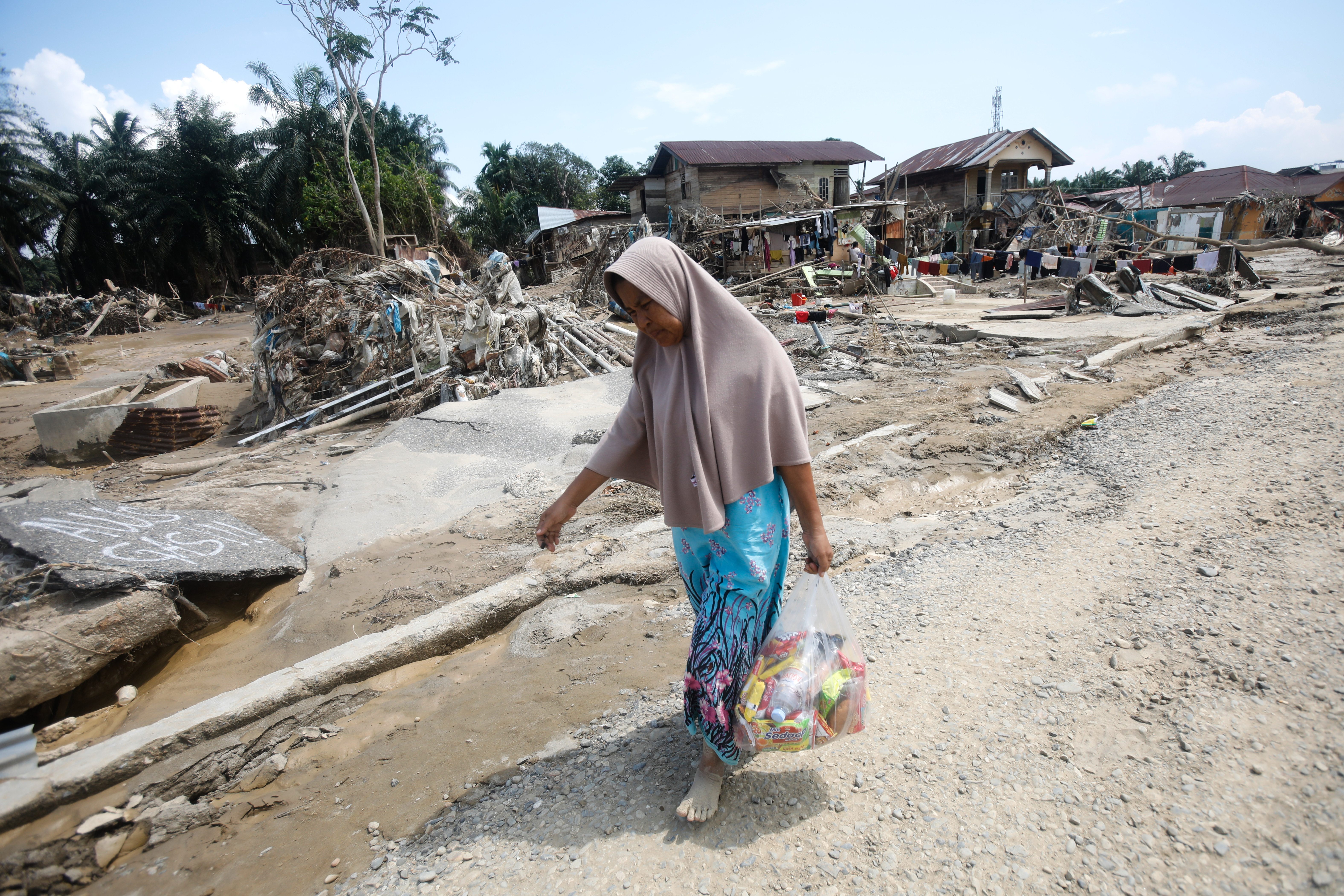 A survivor carries relief goods at an area devastated by flash flooding in Aceh Tamiang on Sumatra Island, Indonesia, Friday, Dec. 5, 2025.
