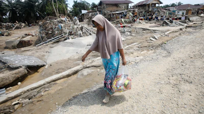 A survivor carries relief goods at an area devastated by flash flooding in Aceh Tamiang on Sumatra Island, Indonesia, Friday, Dec. 5, 2025.