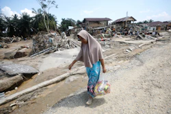 A survivor carries relief goods at an area devastated by flash flooding in Aceh Tamiang on Sumatra Island, Indonesia, Friday, Dec. 5, 2025.
