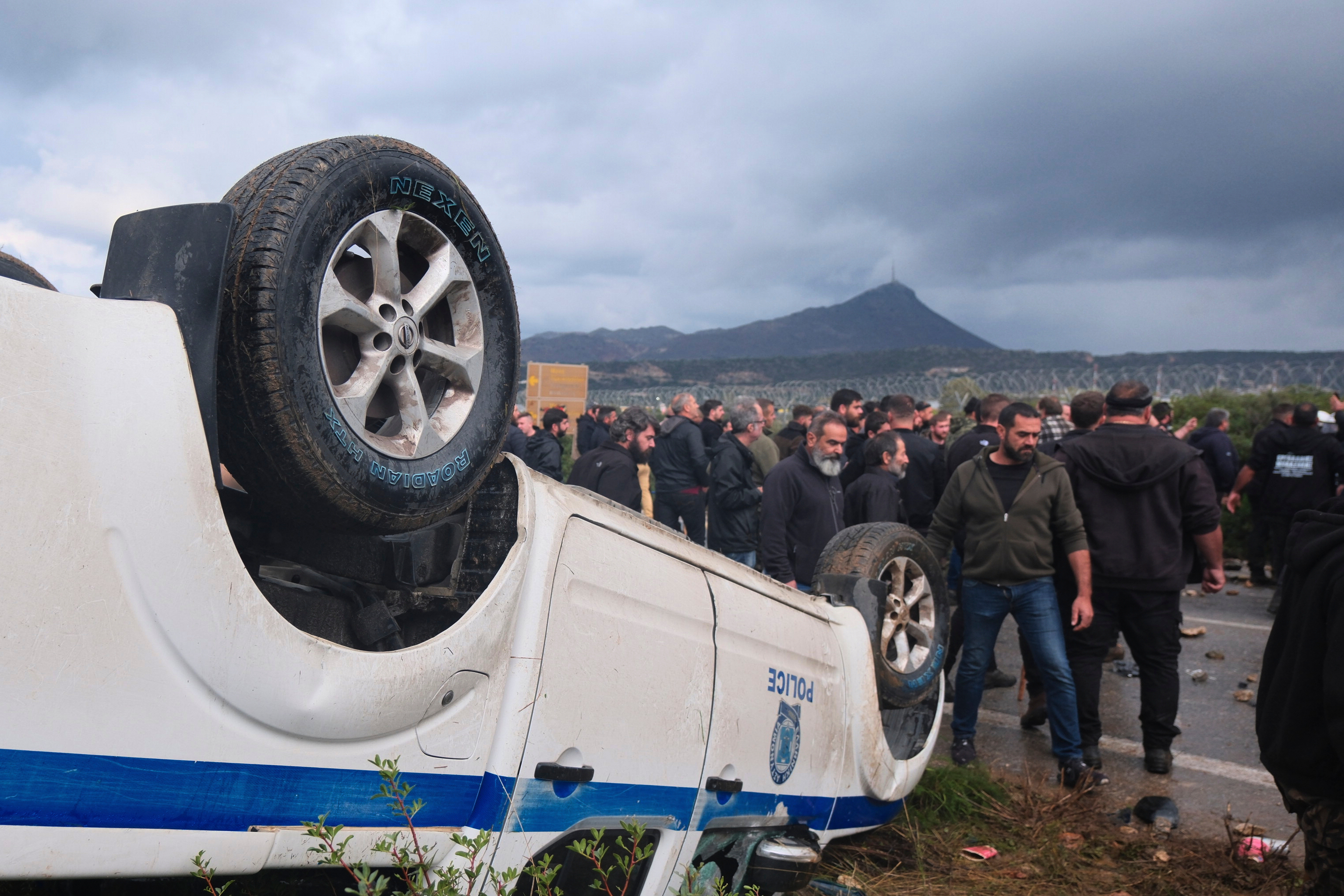 Farmers gather next to an overturned police vehicle during clashes with officers blocking their march to Chania's airport on Crete, Greece, Monday, Dec. 8, 2025, amid protests over delayed EU farm subsidies.