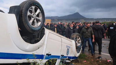 Farmers gather next to an overturned police vehicle during clashes with officers blocking their march to Chania's airport on Crete, Greece, Monday, Dec. 8, 2025, amid protests over delayed EU farm subsidies.