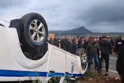 Farmers gather next to an overturned police vehicle during clashes with officers blocking their march to Chania's airport on Crete, Greece, Monday, Dec. 8, 2025, amid protests over delayed EU farm subsidies.