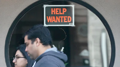 Pedestrians walk past a help wanted sign posted on the door of a restaurant in San Francisco, April 18, 2023.