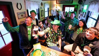 More than a dozen people pose for a photo in a tiny pub rented by Mark Cote, third from right, Andover, Mass., March 13, 2026.