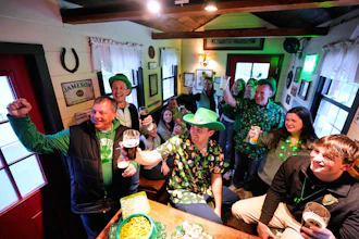 More than a dozen people pose for a photo in a tiny pub rented by Mark Cote, third from right, Andover, Mass., March 13, 2026.