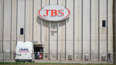 Employees walk in front of the entrance to the JBS meat processing plant, July 23, 2021, in Greeley, Colo.