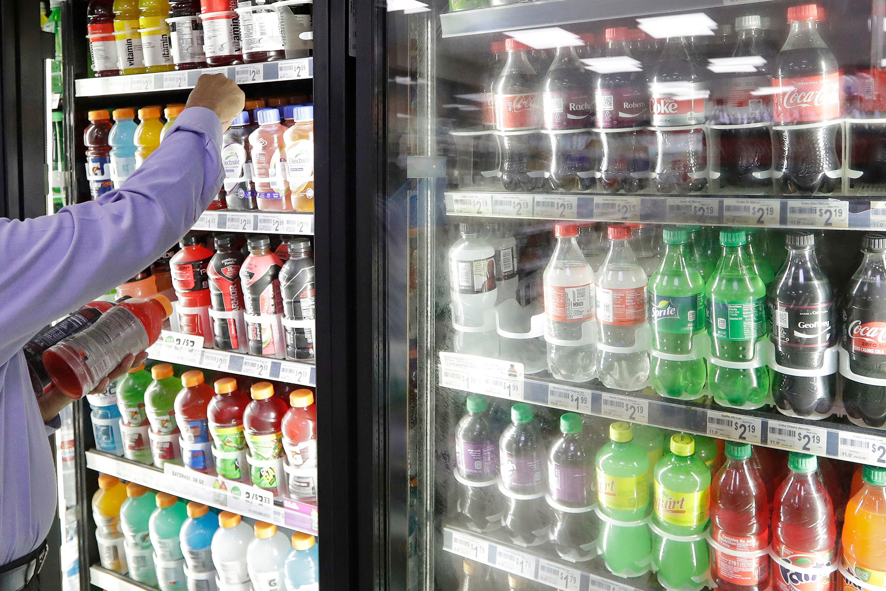 A shop owner reaches into a drink display refrigerator at his convenience store in Kent, Wash., Oct. 1, 2018.