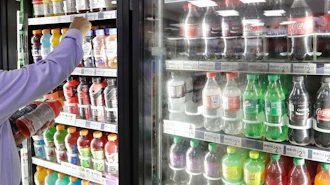 A shop owner reaches into a drink display refrigerator at his convenience store in Kent, Wash., Oct. 1, 2018.