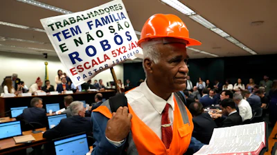 Lawmaker and Pastor Sargento Isidorio holds a sign supporting the end of Brazil's six-day workweek in the Chamber of Deputies, Brasilia, May 27, 2026.